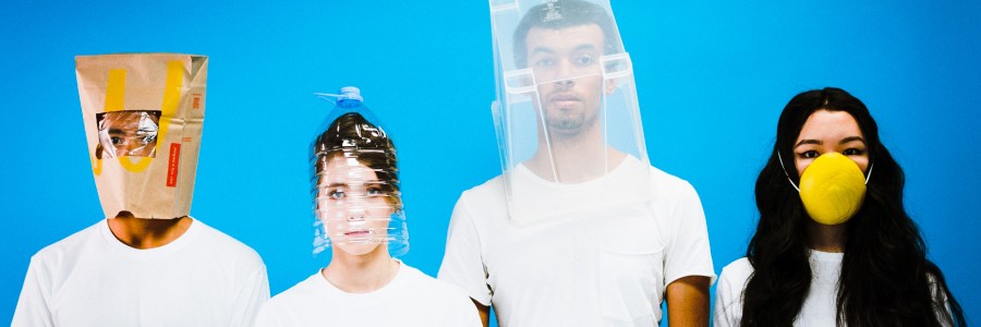 Vier junge Menschen tragen ausgefallene Gesichtsmasken aus Haushaltsgegenständen.