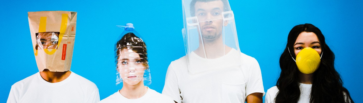 Vier junge Menschen tragen ausgefallene Gesichtsmasken aus Haushaltsgegenständen.