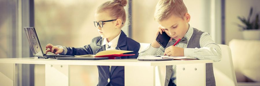 Zwei Kinder im Businesslook mit Telefon und Laptop am Schreibtisch.