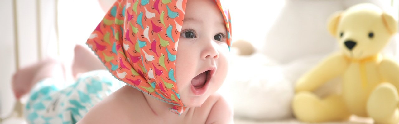 Baby mit Kopftuch auf Spieledecke.
