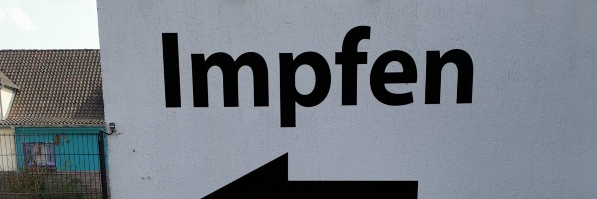 Fensterscheibe mit der Aufschrift "Impfen" und einem Pfeil nach links darunter in einem Impfzentrum.