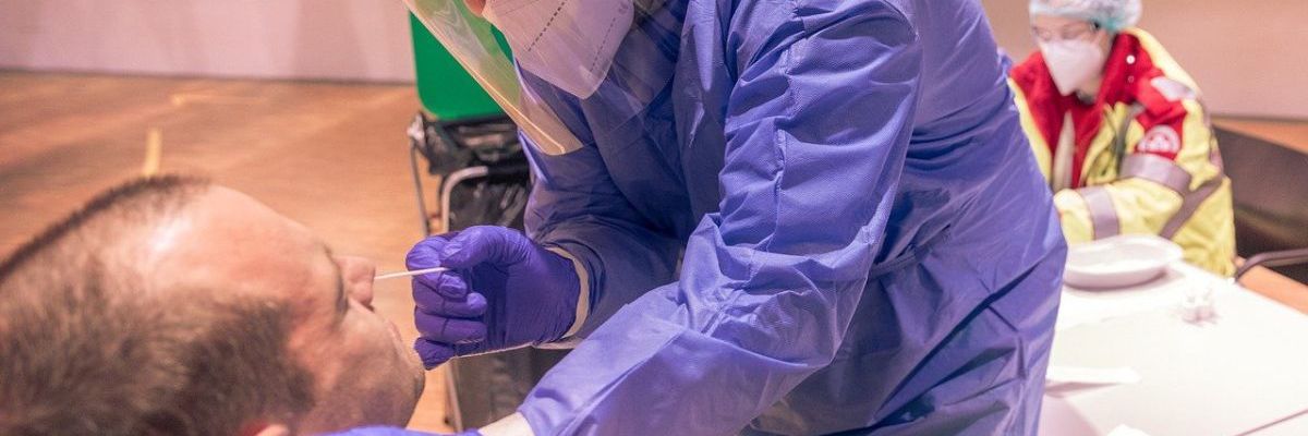 Ein Mann in Schutzanzug nimmt einen Coronaabstrich bei einem anderen Mann vor.