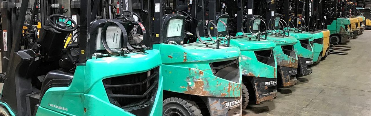 Eine Reihe von türkisen Gabelstaplern steht nebeneinander in einer Hall.