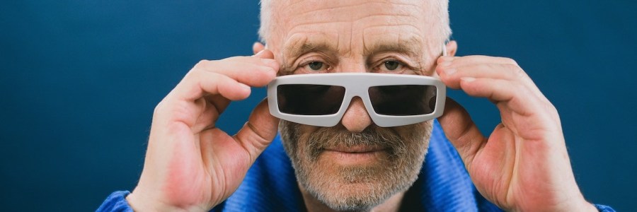 Älterer Mann mit blauer Jacke und weißer Sonnenbrille blickt in die Kamera.