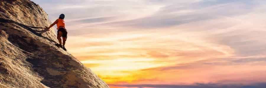 Ein Person erklimmt vor untergehender Sonne einen Berg.
