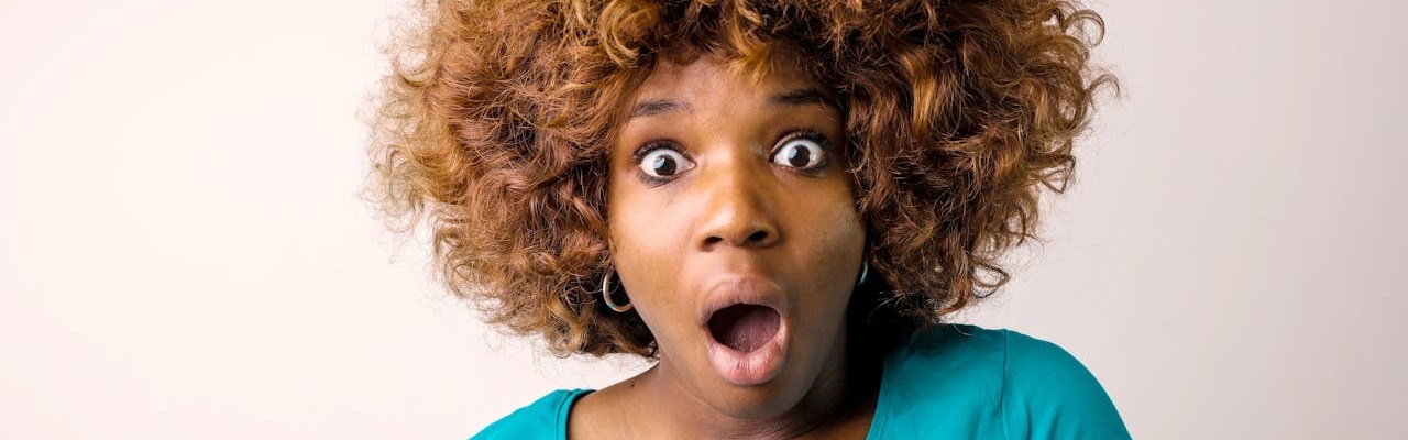 Eine Frau mit türkisem Oberteil blickt erstaunt in die Kamera.