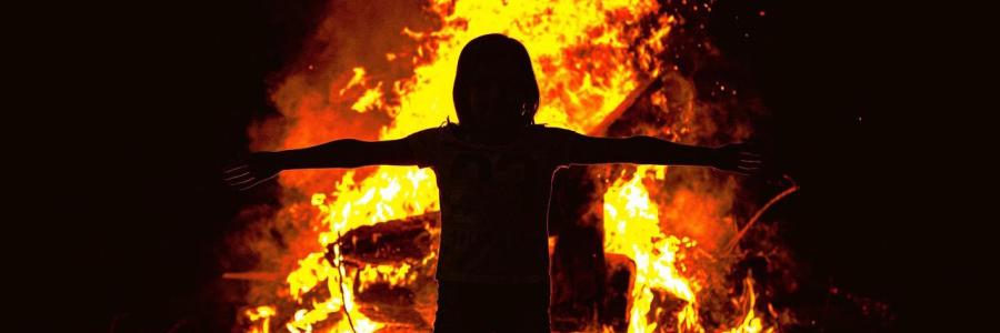 Ein Kind steht mit ausgebreiteten Armen vor einem Osterfeuer.