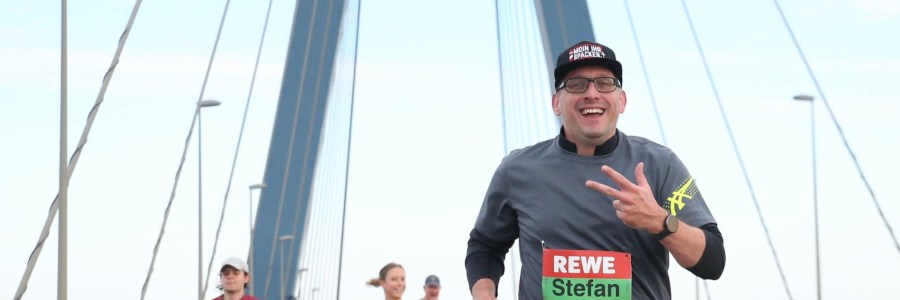 Stefan Kübler zeigt drei Finger und läuft auf einer Brücke.