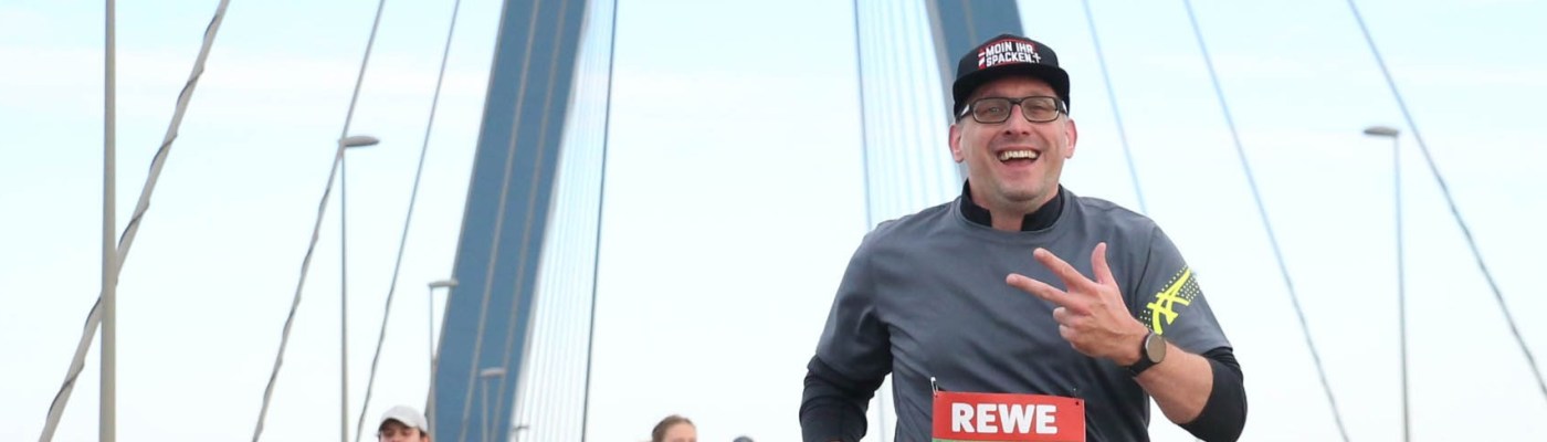 Stefan Kübler zeigt drei Finger und läuft auf einer Brücke.