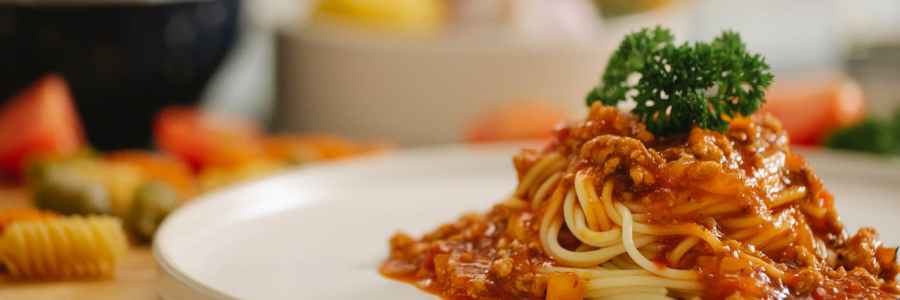 Ein Teller Spaghetti Bolognese auf einem gedeckten Esstisch.