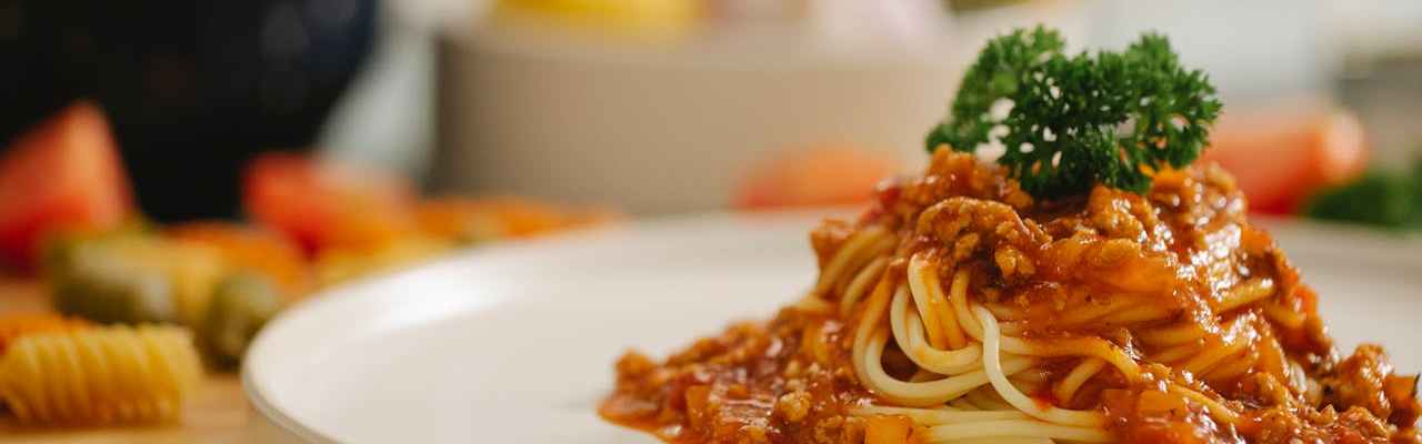 Ein Teller Spaghetti Bolognese auf einem gedeckten Esstisch.