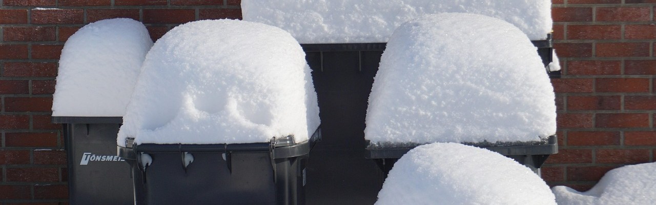 Mülltonnen vor einer Hauswand mit viel Schnee auf dem Deckel.