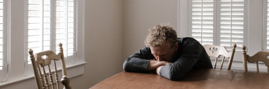 Ein Mann am Tisch mit dem Kopf auf die Hände gesunken.