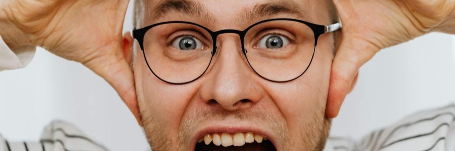 Mann mit Brille hält die Hände an den Kopf und hat den Mund weit aufgerissen.