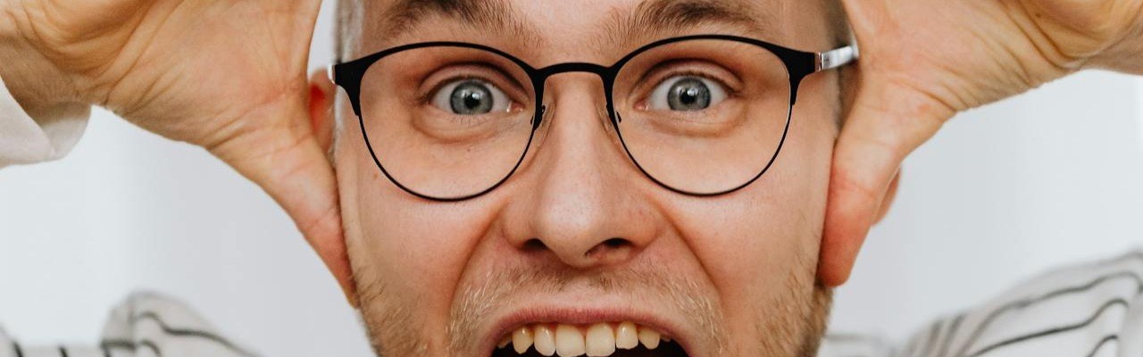 Mann mit Brille hält die Hände an den Kopf und hat den Mund weit aufgerissen.