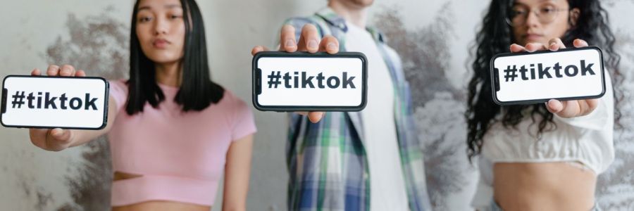 Drei Personen mit Smartphones in der Hand auf denen der Hashtag TikTok steht.